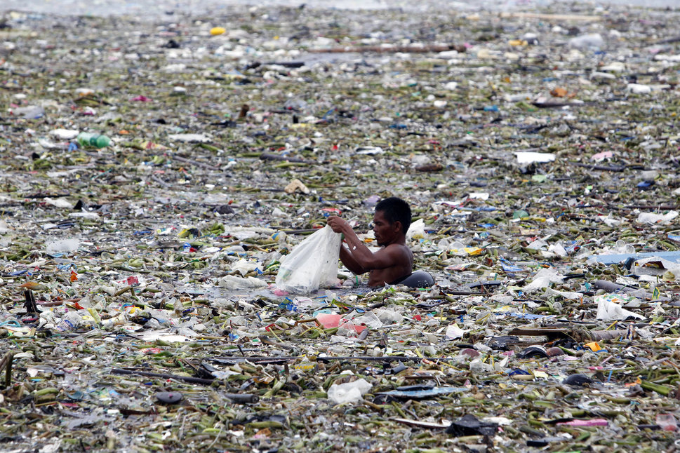 A man collects plastic and other recyclable materials from debris in the waters of Manila Bay after tropical storm Saola hit the Philippine capital
